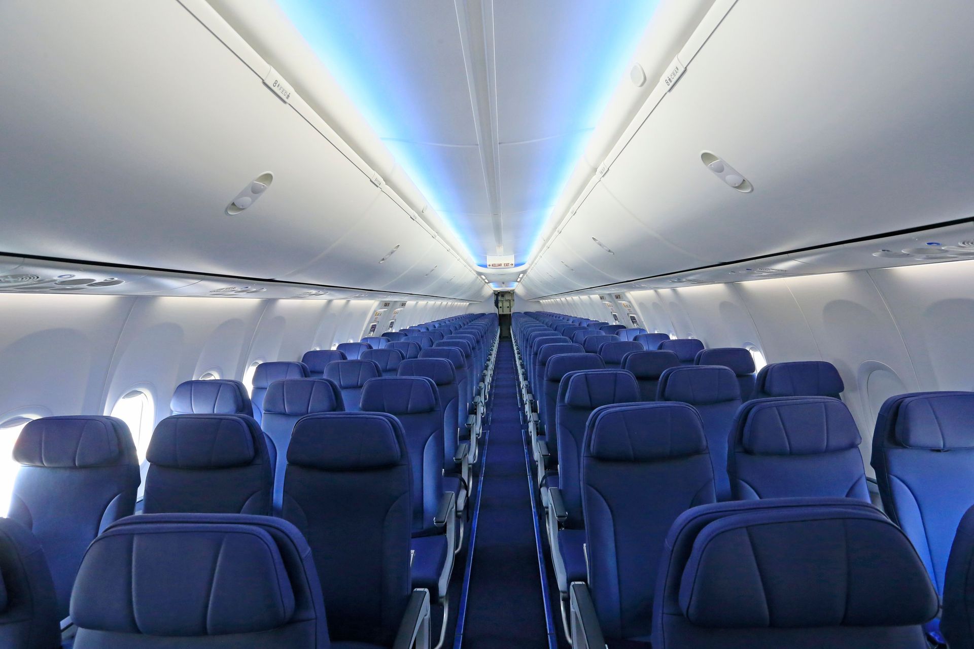 View of an empty airplane cabin with rows of blue seats and ambient lighting.