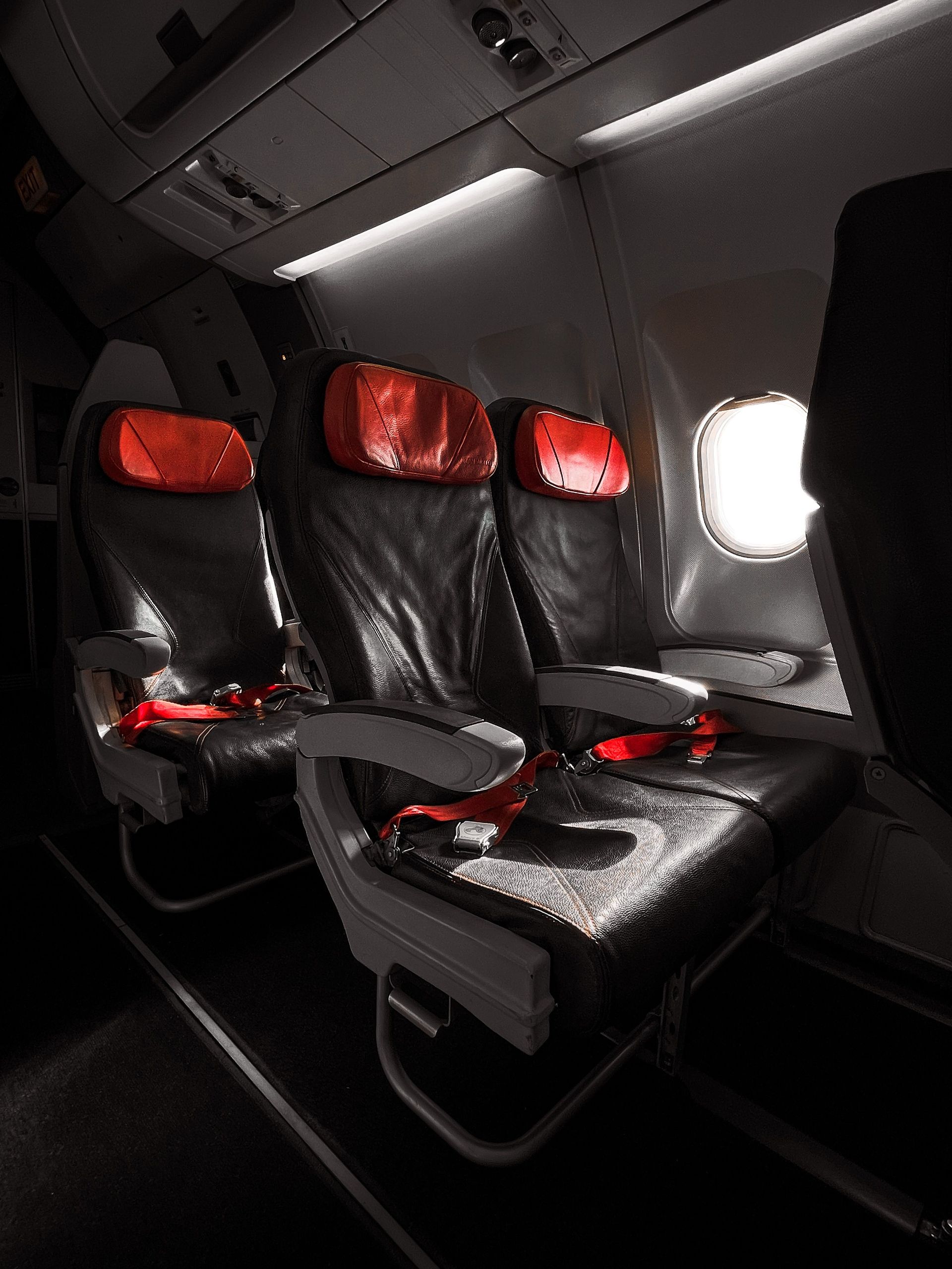 Row of empty airplane seats with red headrests next to a window.